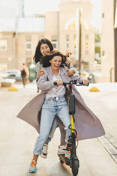 Mutlu yetişkinler eğlenceli arkadaşlar turistler çeşitli kadınlar şehirde scooter 'a biniyor ve günlük kıyafetlerle eğleniyorlar.