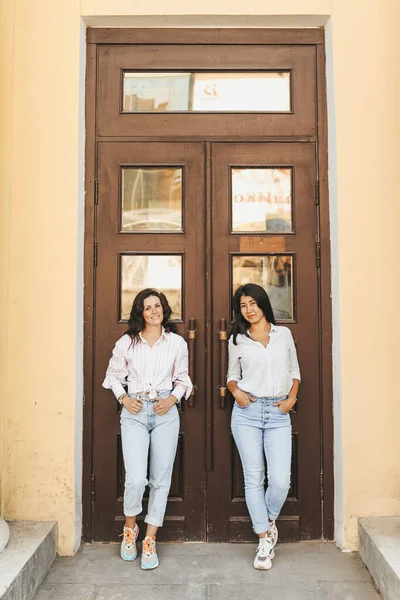 Çok ırklı iki kadın turist kapının önünde dikilip poz veriyorlar.