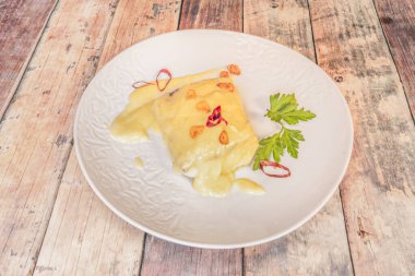 Kremalı morina filetosu, sarımsak ve zeytinyağının mükemmel emülsiyonu, beyaz bir tabakta sunuluyor. 