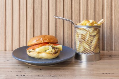 Yanında çörek, duble köfte, buzdağında marul ve arka planda patates kızartması olan bol pastırmalı uzun bir hamburger.