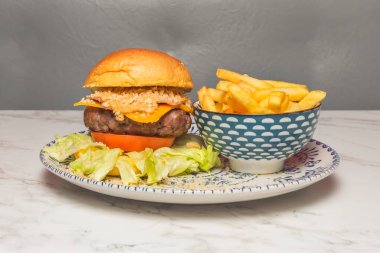 Lezzetli burger, tatlı çörek, sulu biftek, ekmeklenmiş soğan halkaları, ve kayrak tabakta dumanlı barbekü sosu.