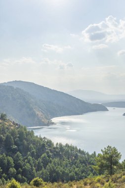 Bir dağ silsilesinin panoramik görüntüsü rüzgarsız bir günde baraj gölünün sakin sularına açıkça yansıyor.