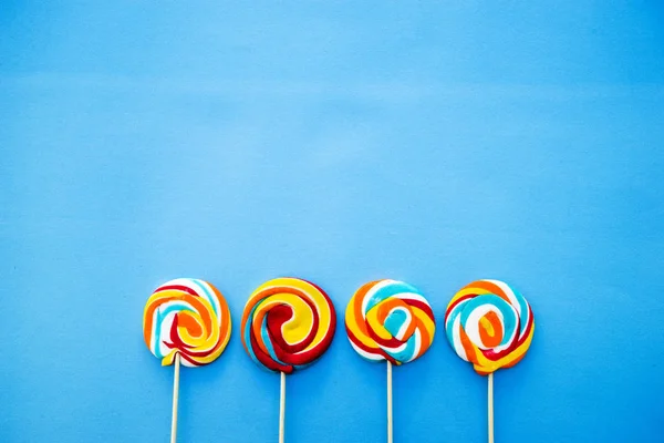 Piruleta de colores sobre un fondo azul. Rayas rojas, blancas y azules en un caramelo. Concepto mínimo. Tienda de dulces serie . — Foto de Stock