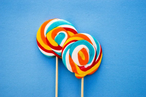 Piruleta de colores sobre un fondo azul. Rayas rojas, blancas y azules en un caramelo. Concepto mínimo. Tienda de dulces serie . — Foto de Stock