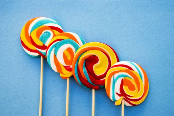 Pirulito colorido sobre um fundo azul. Listras vermelhas, brancas e azuis em um doce. Conceito mínimo. Série de loja de doces . — Fotografia de Stock