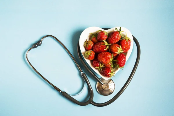 健康の概念。青色の背景色、トップ ビューで聴診器で新鮮なイチゴ. — ストック写真