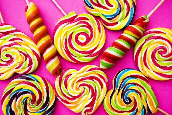 Rainbow lollipop swirl on wooden stick on pink paper background, flat lay