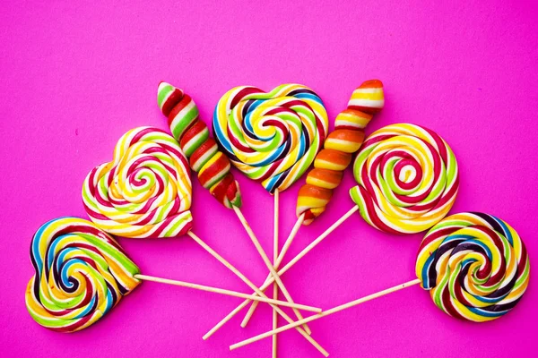 Rainbow lollipop swirl on wooden stick on pink paper background, flat lay