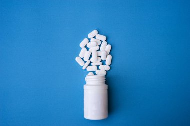 İlaç tabletleri ve ilaç şişeleri mavi arka planda izole edilmiş. Üst görünüm