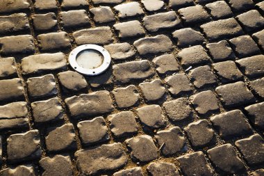 Square lined with cobblestone or stone pavement, walkway or road. The surface of rough stones and rough. Boulders of gray. The cobbles have a mottled pattern and texture.