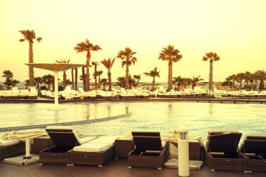 Otel havuzundan güzel bir gün batımı görünüyor. Şemsiye siluetleri ve havuz kenarındaki güneş pansiyonları. Havuzda gün batımı