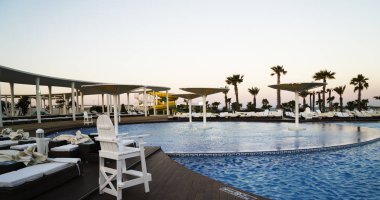 Güzel bir gün batımı, otel havuzundan gün doğumu. Şemsiye siluetleri ve havuz kenarındaki güneş pansiyonları. Havuzda gün batımı