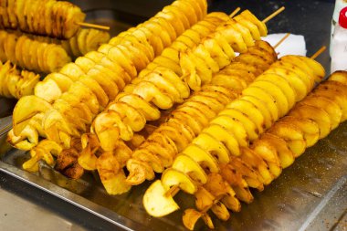 Ahşap çubuk üzerinde sarmal şeklinde patates kızartması. Altın rengi metal tepsi üzerinde piknik sırasında yalan kadar patates kızarmış. Patates chipsy kaşifi