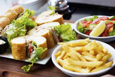 Ekmek, kızarmış patates, yeşillikler ve beyaz tabakta çeşitli sebzeler..