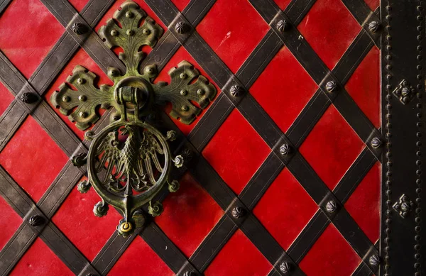 Una manija forjada negra en la puerta de hierro roja. Puerta antigua vintage con asa de hierro . — Foto de Stock