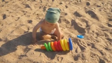 Küçük bir çocuk sahildekumda oynuyor. Bir bebek sürünür ve her yerde çalışırken güler..