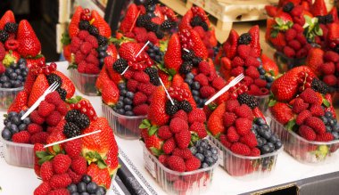 Fresh Berries such as red currant, blackberry, raspberry, strawberry and blueberry in transparent rectangular plastic containers of the same size put in line into a paper pallet ready to sell clipart