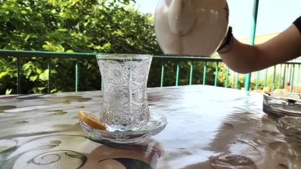 En kvinnlig hand häller te i ett glas från en tekanna på ett bord på gården. — Stockvideo