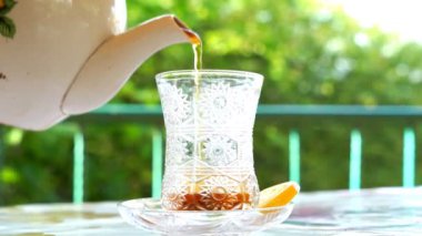 Bir kadının eli, avludaki bir çaydanlıktan bardağa çay doldurur.