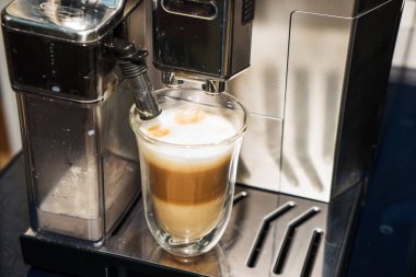 Kahve makinesi, cam bardağa sütlü espresso döker. Cappuccino yapma işlemi.
