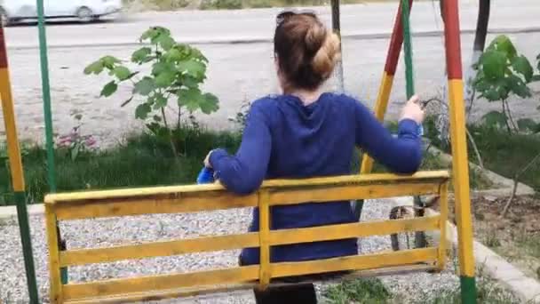 Une fille se balance sur une balançoire en bois. La vue de l'arrière. — Video