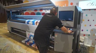 Bakü, Azerbaycan-20 Haziran 2019: Erkek bir kameraman büyük formatlı bir yazıcıya fotoğraf basıyor. Büyük bir biçimli yazıcı mürekkep püskürtme aygıtı makinesi hareket eden beyaz sayfa renk sözlüğü yazdırma ortamı