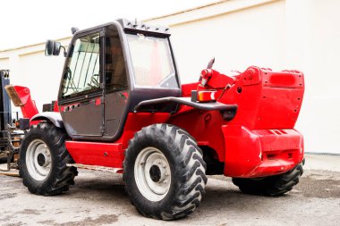 Bahçedeki engebeli bir arazide kırmızı bir forklift duruyor.