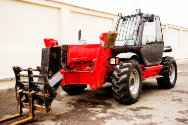 Bahçedeki engebeli bir arazide kırmızı bir forklift duruyor.