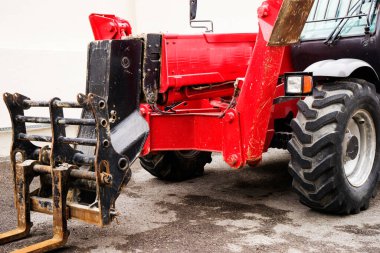 Bahçedeki engebeli bir arazide kırmızı bir forklift duruyor.