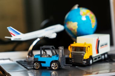 Çevrimiçi alışveriş kavramı için lojistik ve tedarik zinciri yönetimi: dünya, beyaz sarı kamyon, uçak, dizüstü bilgisayardaki forklift, mal veya ürünlerin teslimini resmediyor.