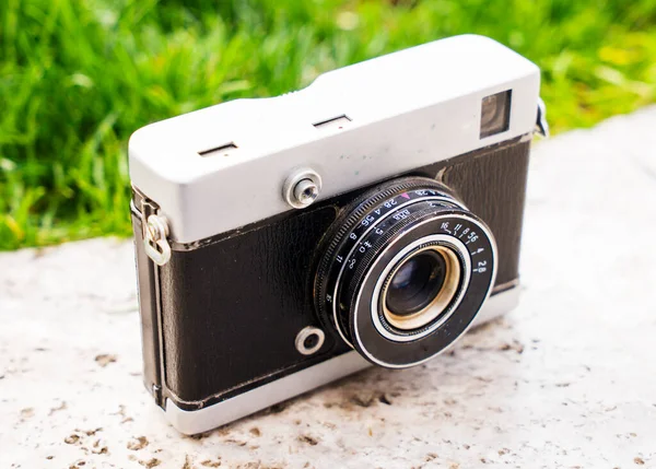 Doğanın bulanık arka planında, bir kaya üzerinde eski bir Sovyet film kamerası. Kameraya odaklanmış sığ alan derinliği. Açık havada. Retro resim biçimi.