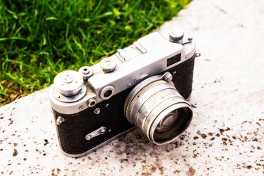 Doğanın bulanık arka planında, bir kaya üzerinde eski bir Sovyet film kamerası. Kameraya odaklanmış sığ alan derinliği. Açık havada. Retro resim biçimi.