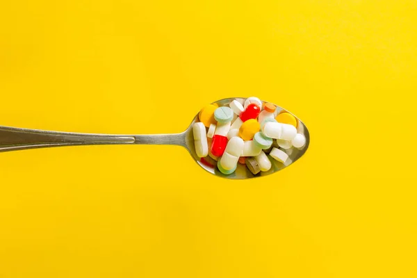 Spoon full of pills on a yellow background. Self-medication and drug abuse concept.