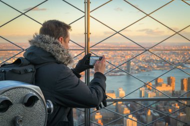Cep telefonu ile bir resim çekerken New York'un bir çatı üzerinde gün batımı zevk Adam