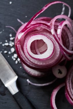 Close-up dilimlenmiş kırmızı İspanyolca soğan halkaları ve siyah arduvaz kesme tahtası - düz yatıyordu görünümü üzerinde deniz tuzu. Sağlıklı organik vejetaryen yemek veya yemek hammaddelerini