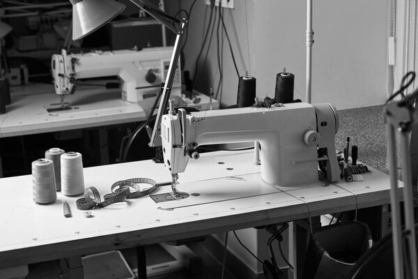 Professional seamstress working space with sewing machine, thread spools and measure tape on the table. Tailor atelier - handmade exclusive clothes making and repair, private business concept