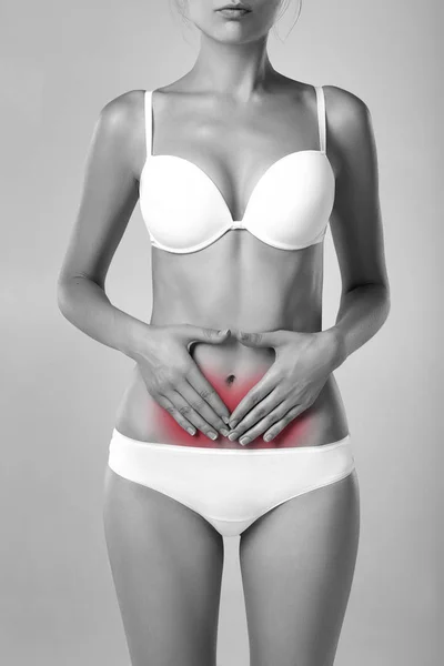 Black and white monochrome photo of female with fit slim body suffering from pain and holding her hands on the marked red ache hearth. Digestive disorders, period pain, health issues concept