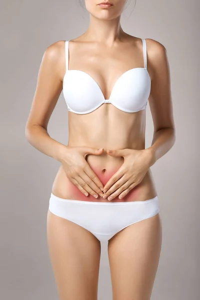 Close-up of female with fit slim body in panties and bra suffering from pain and holding her hands on the marked red ache hearth. Digestive disorders, period pain, health issues concept — Stock Image Close Female Fit Slim Body Panties Bra Suffering Pain Holding Royalty Free Stock Photos