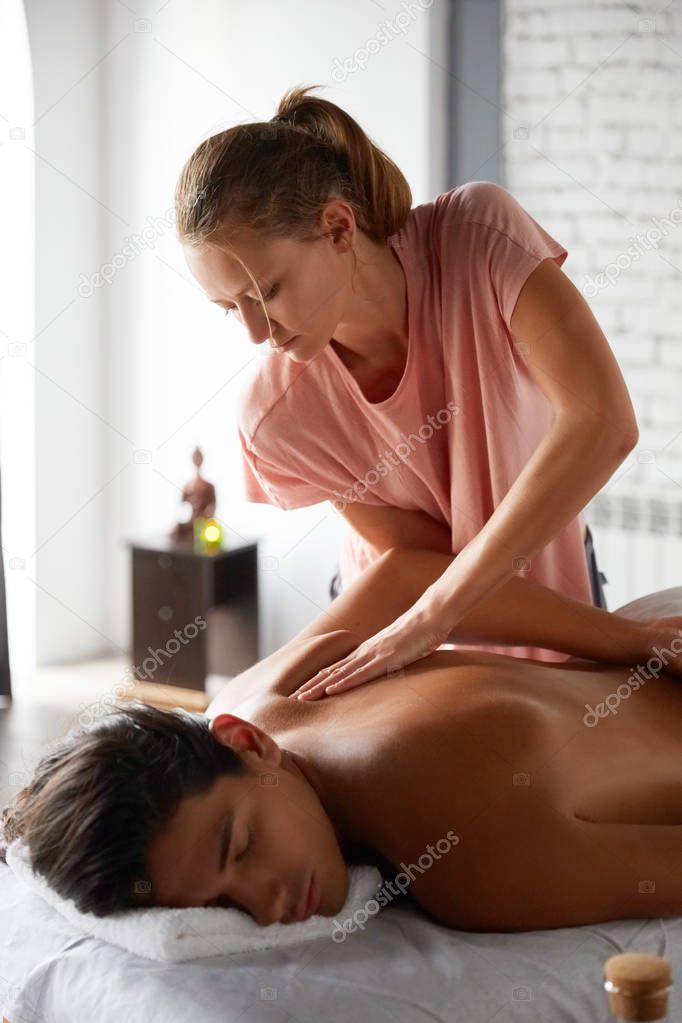 Close up shot of a professional masseuse doing massage with forearms and cubits for male client. Young man relaxing receiving facial massage at the spa center. Relaxation therapy resort recreation.