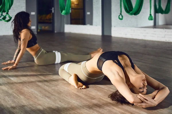 The interior shooting of an two women practices different inversion antigravity yoga with a hammock in yoga studio. The balance between mental and physical, one person effort and achievement concept