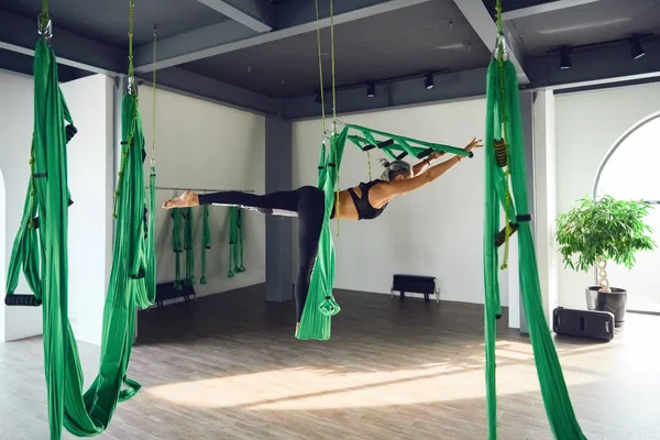 The interior shooting of an adult woman practices different inversion antigravity yoga with a hammock in yoga studio. The balance between mental and physical, one person effort and achievement concept