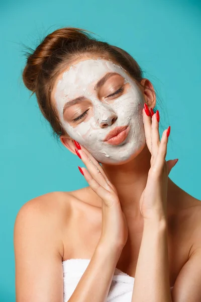Beauty treatment - woman applying clay face mask
