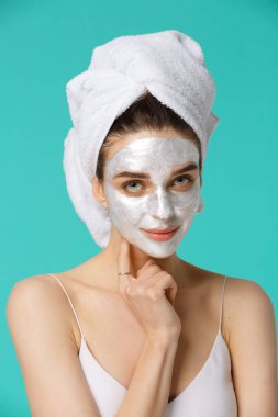 Kafasına havluyla sarılmış gümüş parıltılı yüz maskesi takan ve eğlenen genç bir kadın. Günlük sabah rutini - yüz temizleme, cilt bakımı, kabuk soyma, nemlendirici ve güzellik tedavi konsepti