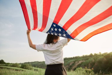 4 Temmuz. 4 Temmuz 'da. Amerikan bayrağıyla güzel bir simgeye karşı Amerikan bayrağı taşıyan bir kadın. Bağımsızlık Günü. Güzel gün batımı ışığı. Vatansever bayram, demokrasi saygı ve gazi saygı kavramı