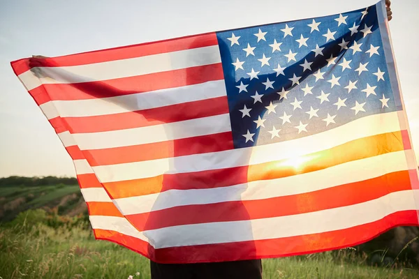 4th of July. Fourth of July. American woman with the national American flag against beautiful landmark. Independence Day. Beautiful sunset light. Patriotic holiday, democracy respect and veteran respect concept