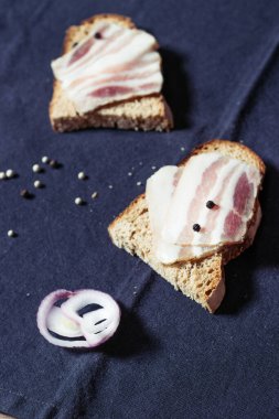 Ahşap masadaki masa örtüsünün üzerinde domuz yağlı ve siyah ekmekli sandviç.