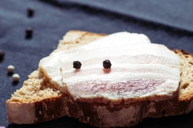 Ahşap masadaki masa örtüsünün üzerinde domuz yağlı ve siyah ekmekli sandviç.