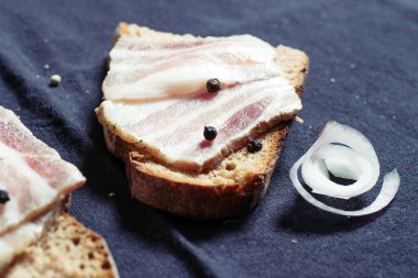 Ahşap masadaki masa örtüsünün üzerinde domuz yağlı ve siyah ekmekli sandviç.