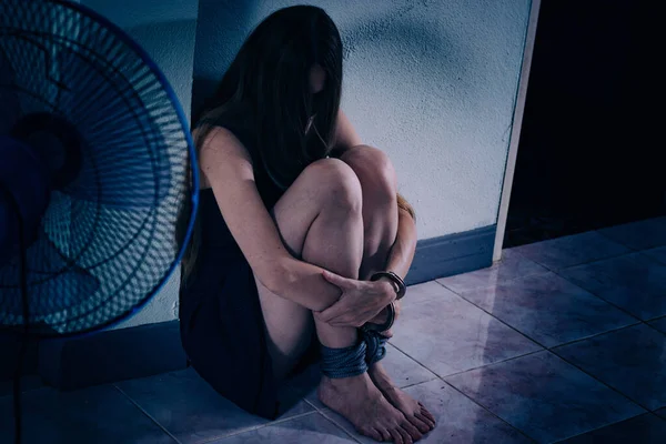 Genç bir kadın şiddete maruz kalıyor, yere oturuyor, ellerini kelepçeleyerek yüzünü kapatıyor. Elleri damarlar ve yaralar, bacakları bir iple bağlanmış. Travma sonrası stres bozukluğu.