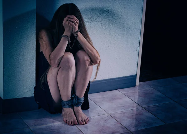 Genç bir kadın şiddete maruz kalıyor, yere oturuyor, ellerini kelepçeleyerek yüzünü kapatıyor. Elleri damarlar ve yaralar, bacakları bir iple bağlanmış. Travma sonrası stres bozukluğu.